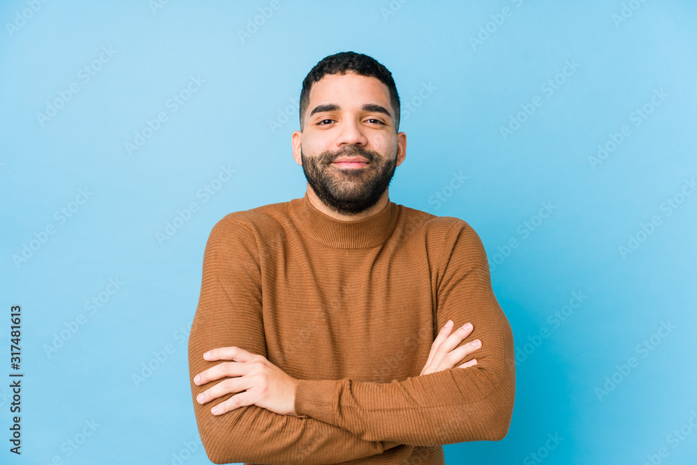 Young latin man against a blue background isolated who feels confident, crossing arms with determination. Young latin man against a blue background isolated who feels confident, crossing arms with determination.