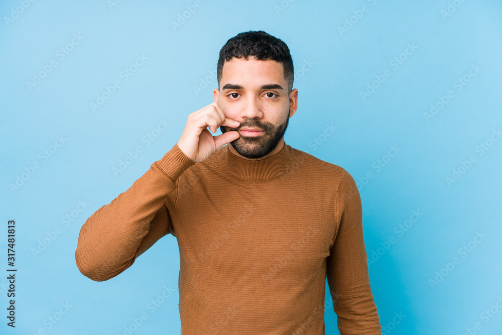 Young latin man against a blue background isolated with fingers on lips keeping a secret. Young latin man against a blue background isolated with fingers on lips keeping a secret.