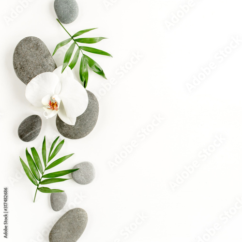 Spa stones, palm leaves, flower white orchid and zen like grey stones on white background. Flat lay, top view