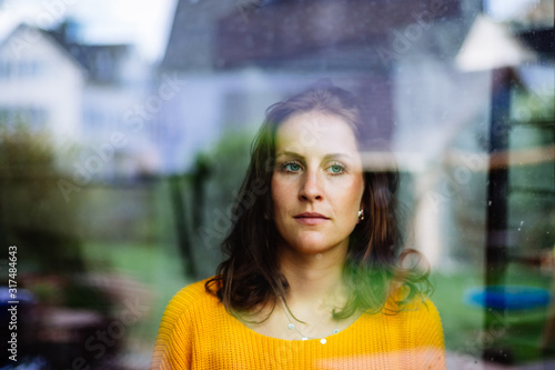 Young woman looks thoughtfully and sadly through the window into the garden with children's toys