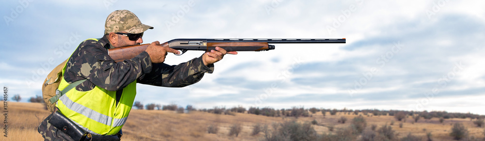 Fototapeta premium Hunter man in camouflage with a gun during the hunt in search of wild birds or game. Autumn hunting season.