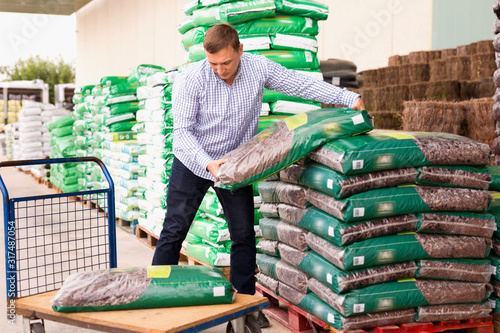 Obraz na płótnie Man choosing compost soil in plastic bags in hypermarket