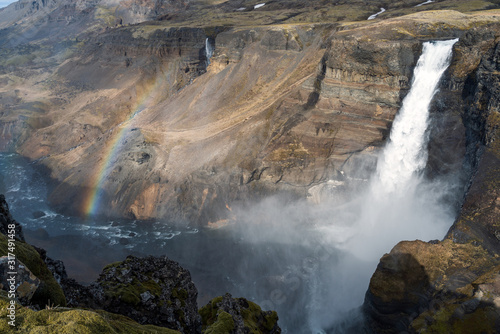 Closeup shot of the colorful and textured volcanic rocks with Haifoss waterfall and rainbow next to it. Porsadalur area in Iceland. Nature and landscapes concept.