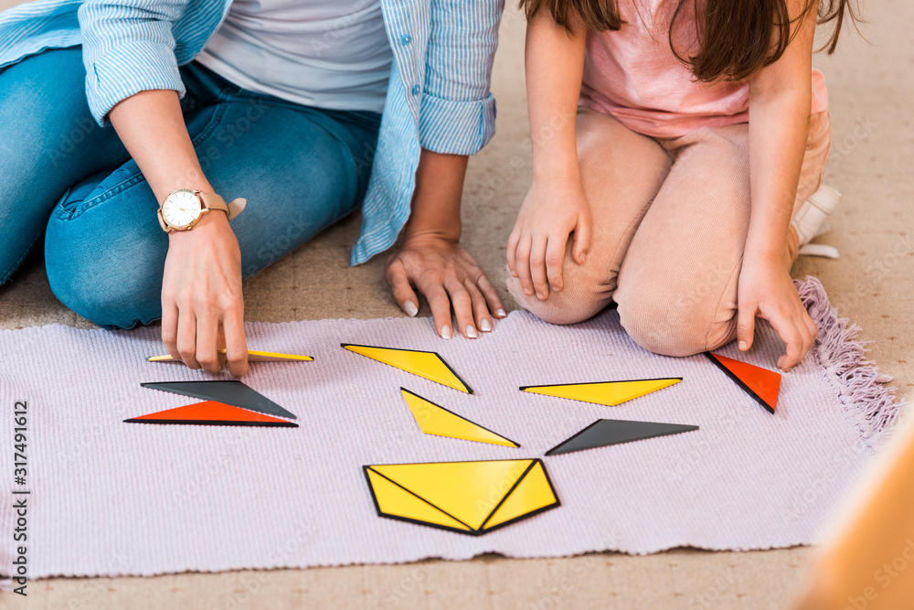 Cropped view of kid and teacher playing educational game on floor in montessori class Cropped view of kid and teacher playing educational game on floor in montessori class