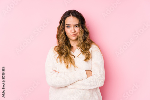 Young curvy woman posing in a pink background isolated frowning face in displeasure, keeps arms folded.