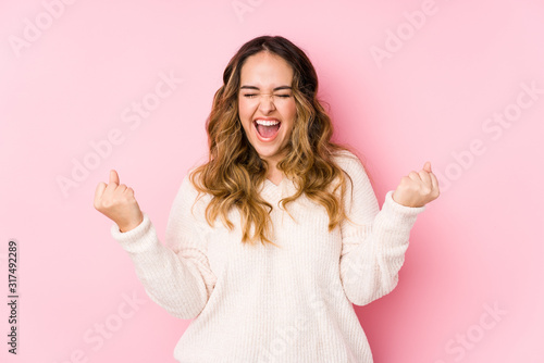 Young curvy woman posing in a pink background isolated cheering carefree and excited. Victory concept. photo