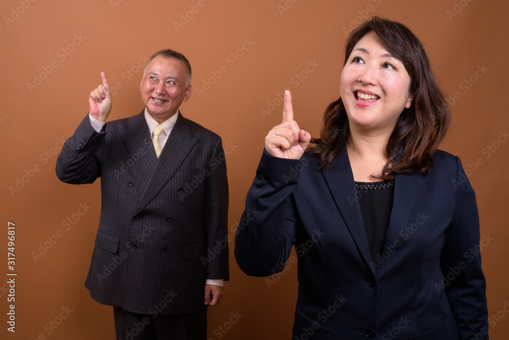 Happy mature Asian businessman and mature Asian businesswoman pointing up together Happy mature Asian businessman and mature Asian businesswoman pointing up together