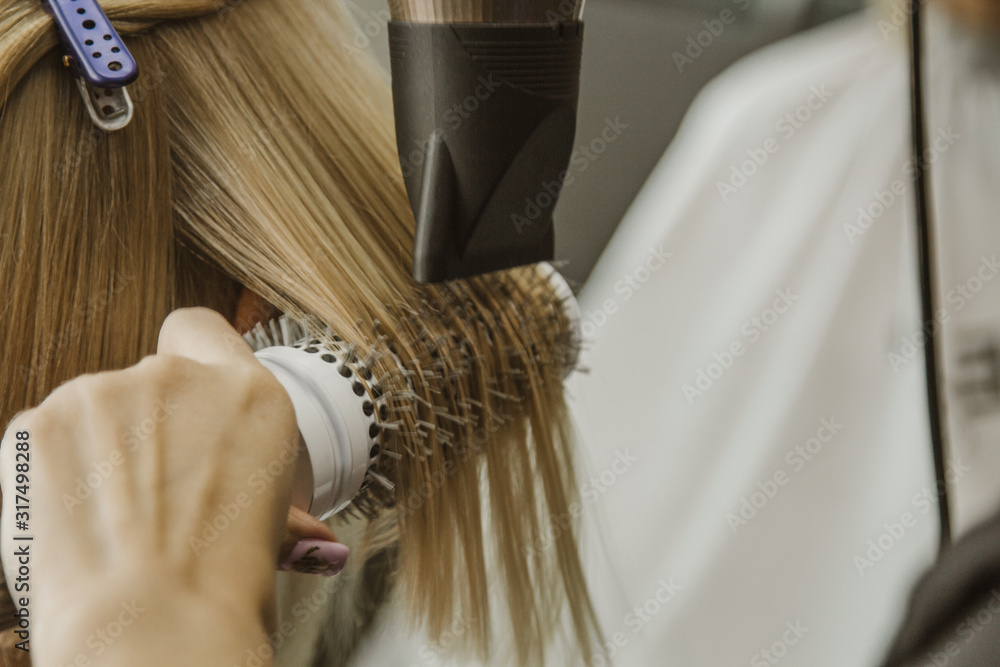 Naklejka premium Close up of hairdresser hands drying human hair with equipment. Woman holding a comb. close-up. Macro photo.