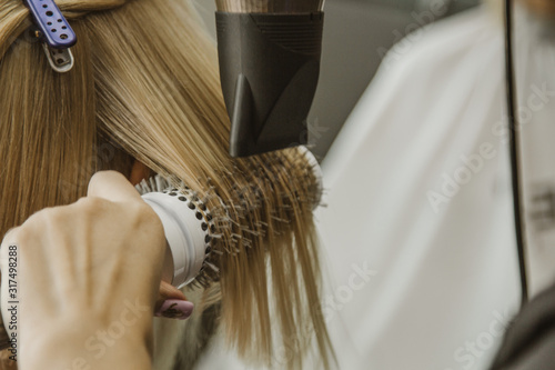 Close up of hairdresser hands drying human hair with equipment. Woman holding a comb. close-up. Macro photo.