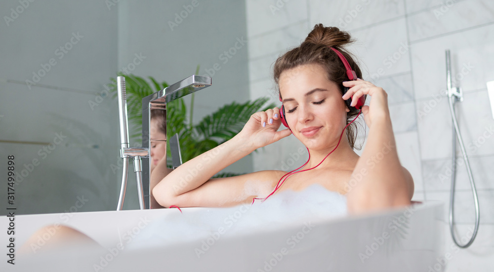 Girl with headphones listening to music while taking bath with soap