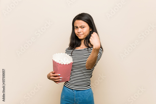 Young asian girl holding a popcorn bucket showing fist to camera, aggressive facial expression.