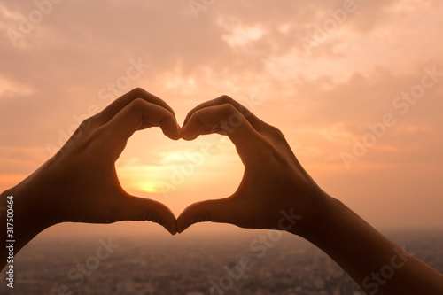 A hands in the form of heart love. Sign of valentine day at sunset with landscape view of city