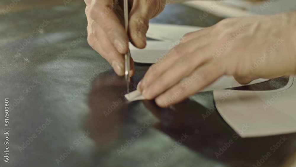 Hands of craftsman placing a pattern on the piece of clak leather and cutting it with razor around. Hands of craftsman placing a pattern on the piece of clak leather and cutting it with razor around.
