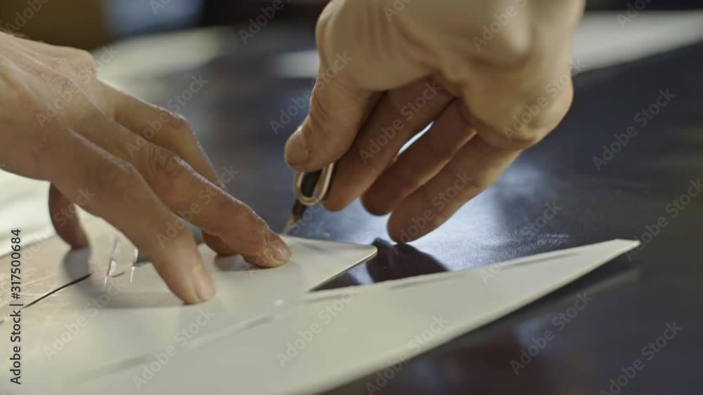 Hands of craftsman placing a pattern on the piece of clak leather and cutting it with razor around. Hands of craftsman placing a pattern on the piece of clak leather and cutting it with razor around.