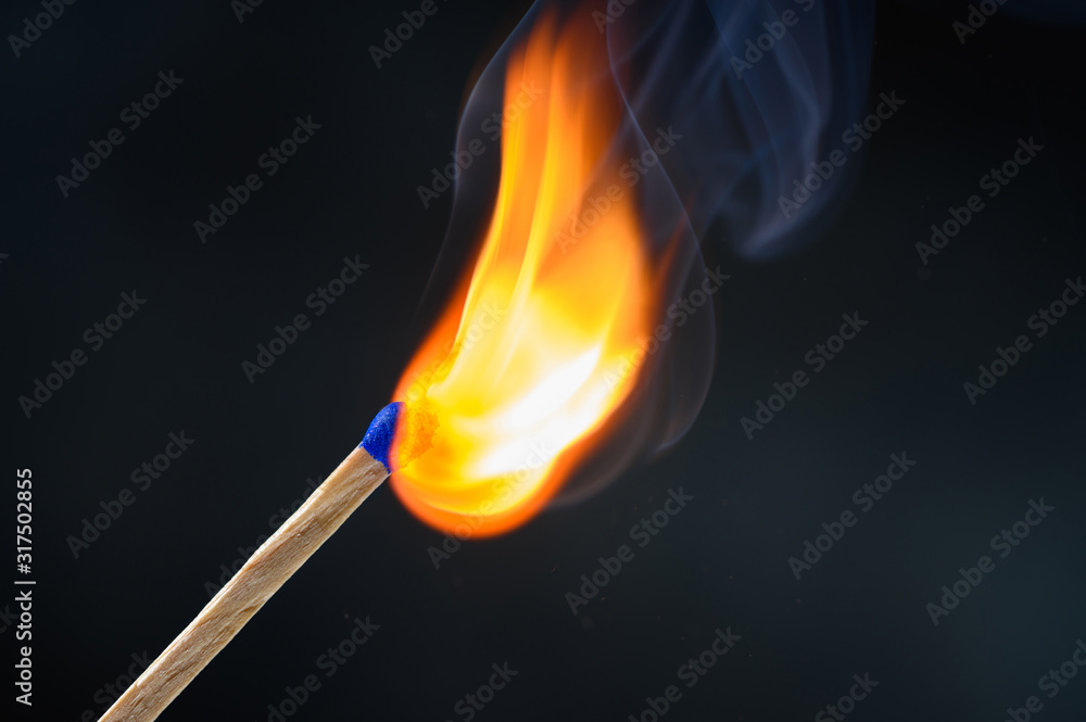 Wooden match stick with blue head ignited and burning bright big fire on black background.