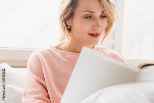 Cconcentrated young woman under blanket reading book.