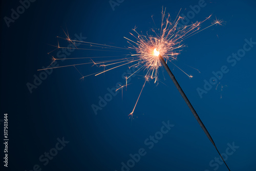 Burning festive Christmas sparkler on blue background with a lot of sparks