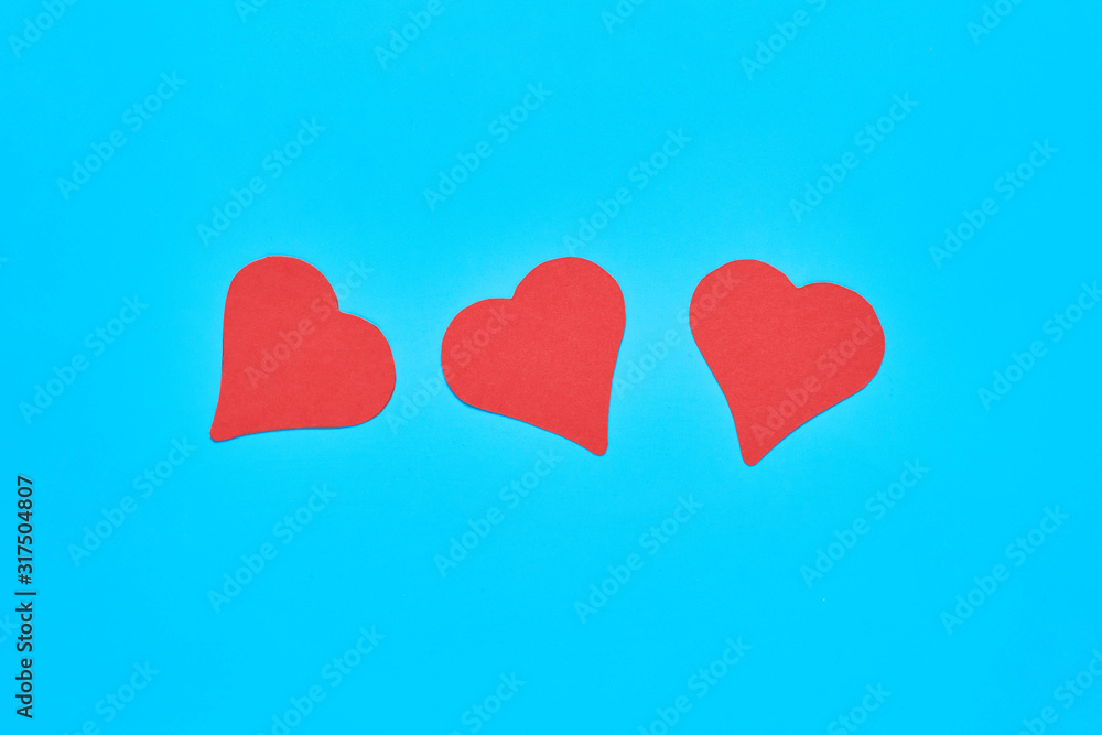 Row of three red paper hearts on blue background. Concept of Valentines Day. Top view. Close-up