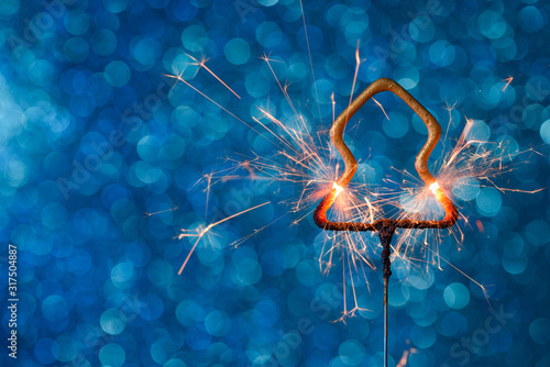 Burning sparkler in christmas new year tree shape over blue glitter background with copy-space.
