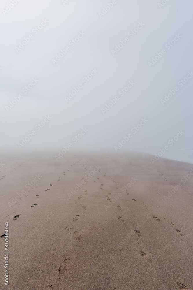 Ocean beach in dense fog with footprints on sand leading nowhere Ocean beach in dense fog with footprints on sand leading nowhere