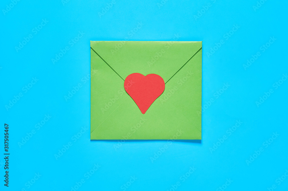 Closed green postal envelope and red paper heart on blue desk. Love message. Concept of Valentines Day. Top view. Close-up Closed green postal envelope and red paper heart on blue desk. Love message. Concept of Valentines Day. Top view. Close-up
