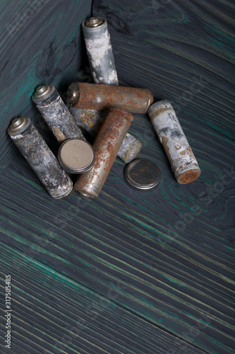 Spent finger-type batteries coated with corrosion. They lie on brushed pine boards painted in black and green.