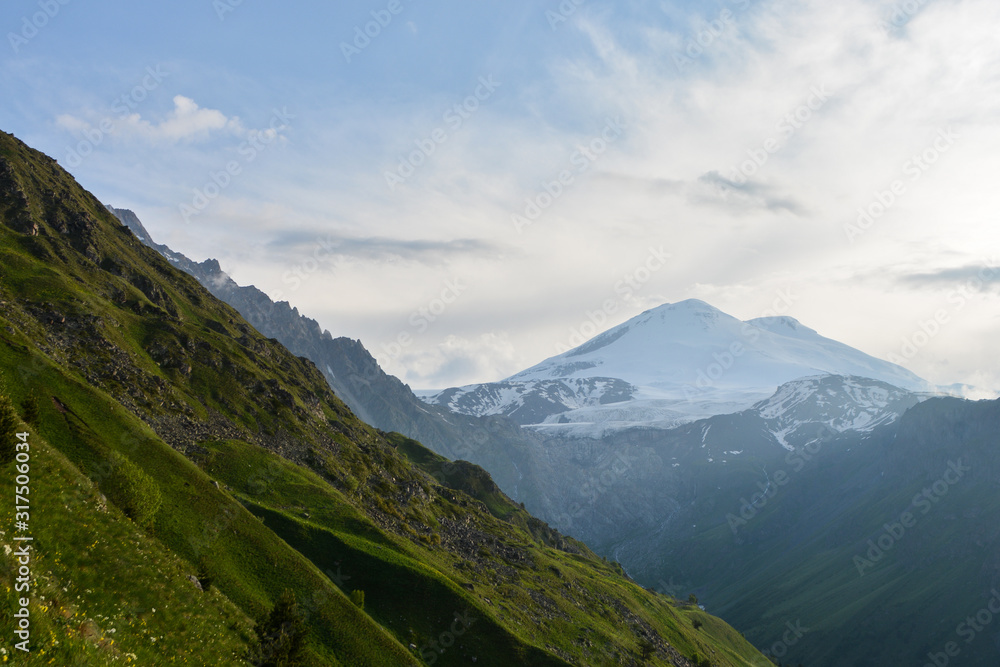 huge snow mountain Elbrus in the distance at sunset with greenery and small trees in the foreground and a glacier with waterfalls of clean drinking water