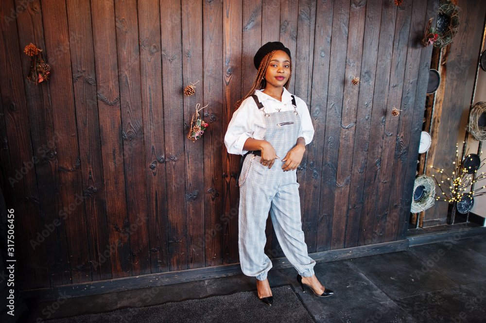 African american woman in overalls and beret against wooden wall.