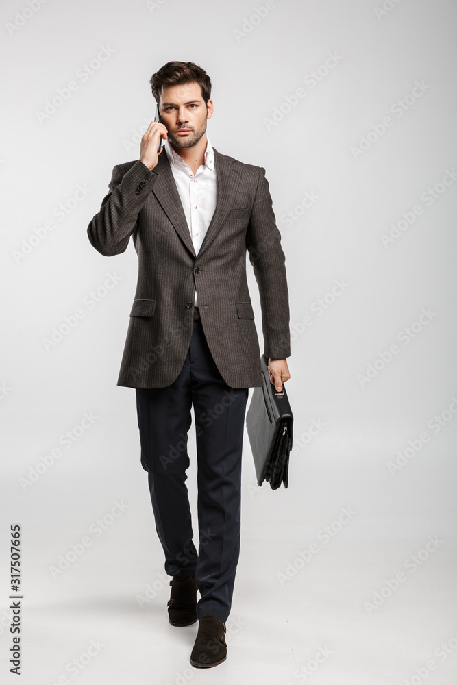 Image of young businessman using cellphone while walking with bag Image of young businessman using cellphone while walking with bag