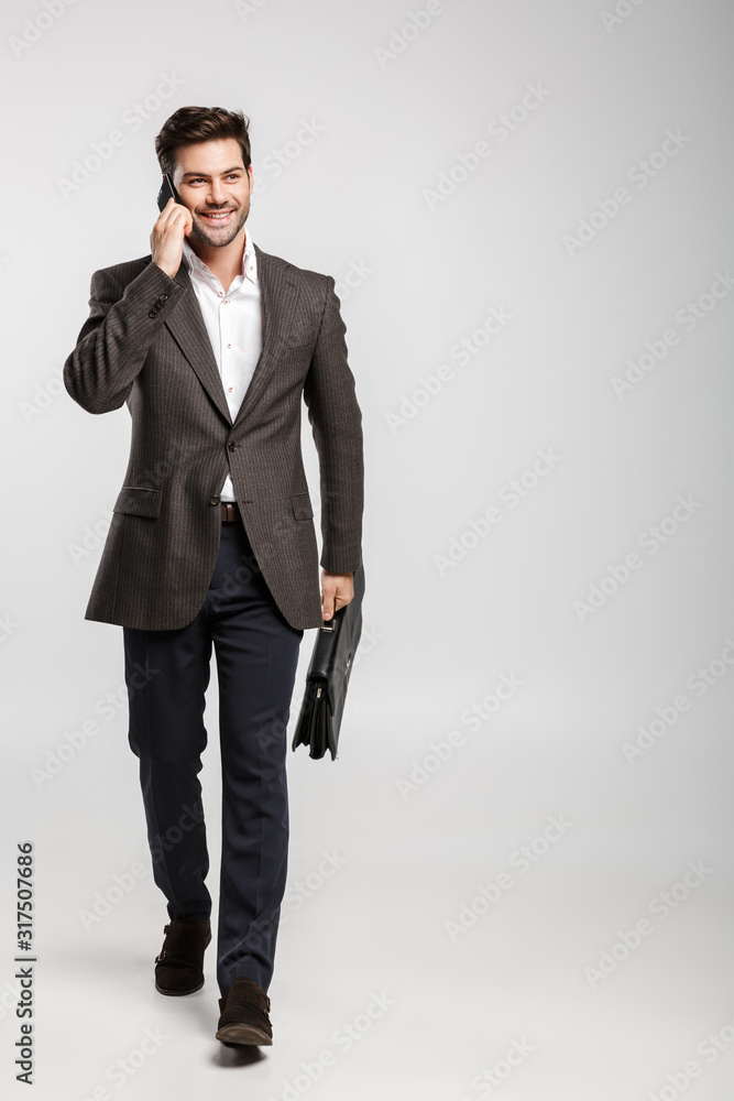 Image of young smiling businessman talking on cellphone while walking with bag Image of young smiling businessman talking on cellphone while walking with bag