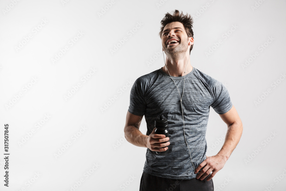 Image of young laughing man using earphones and holding water bottle Image of young laughing man using earphones and holding water bottle