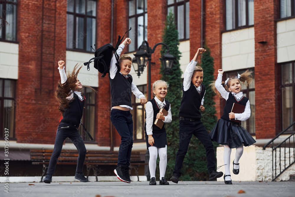 Group of kids in school uniform jumping and having fun outdoors together near education building