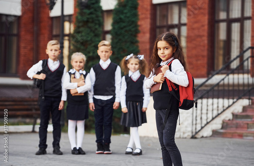 Group of kids in school uniform posing to the camera outdoors together near education building