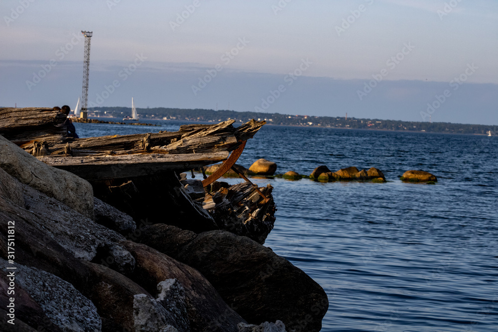 A broken boat at the wharf amid the opposite coast; The boat is stuck with chips and metal rivets