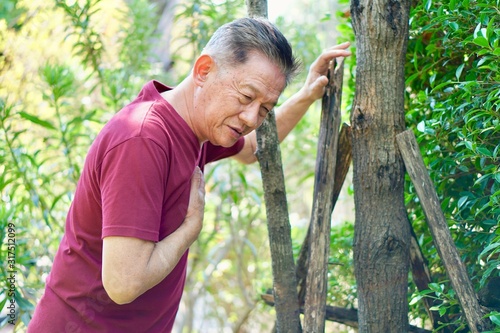 An old asian man in red t shirt getting chest pain standing in the garden