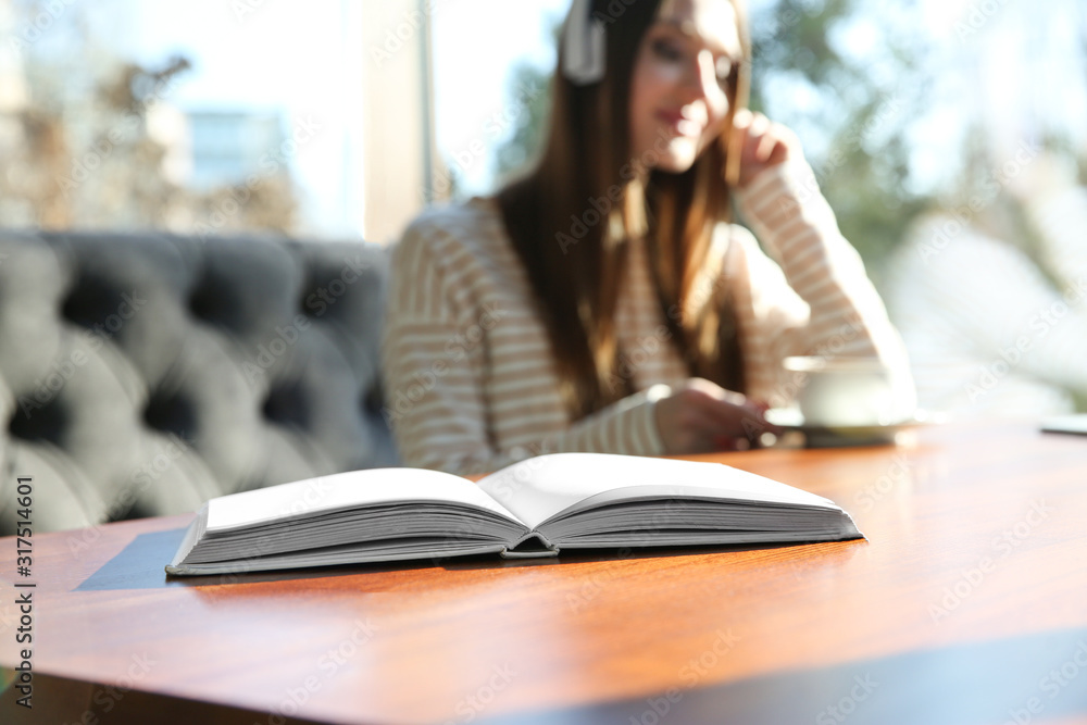 Book on table in cafe and woman with headphones on background. Audiobook concept Book on table in cafe and woman with headphones on background. Audiobook concept