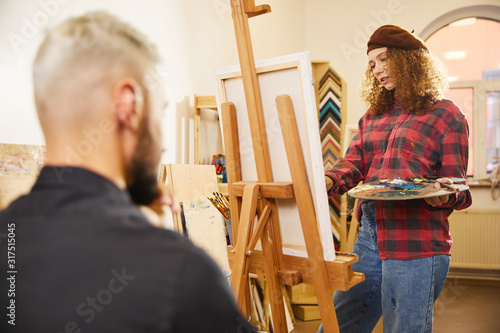 Curly girl is drawing a portrait of a man sits before her