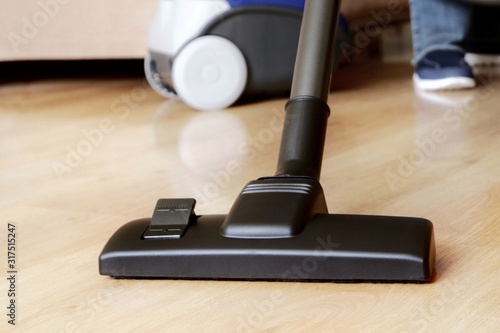 Close-up modern vacuum cleaner over wooden parquet floor background.Vacuuming, housekeeping and cleaning concept.