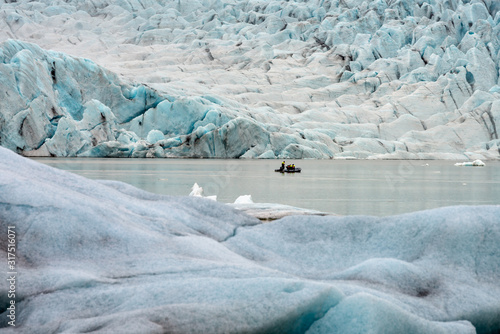 People in little inflatable rubber boat close to Vatnajokull glacier in Fjallsarlon glacier lagoon in Iceland. Melting ice and ice chunks floating around. Climate change concept. photo