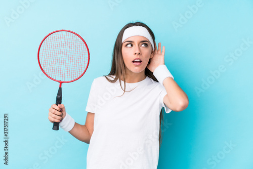 Young caucasic woman playing badminton isolated trying to listening a gossip. © Asier
