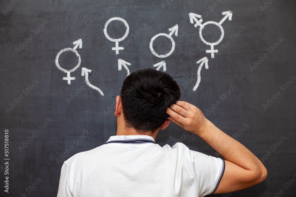 A man makes a choice at a chalk Board with gender symbols. A symbol of transgender and female and male gender symbols on a chalkboard.