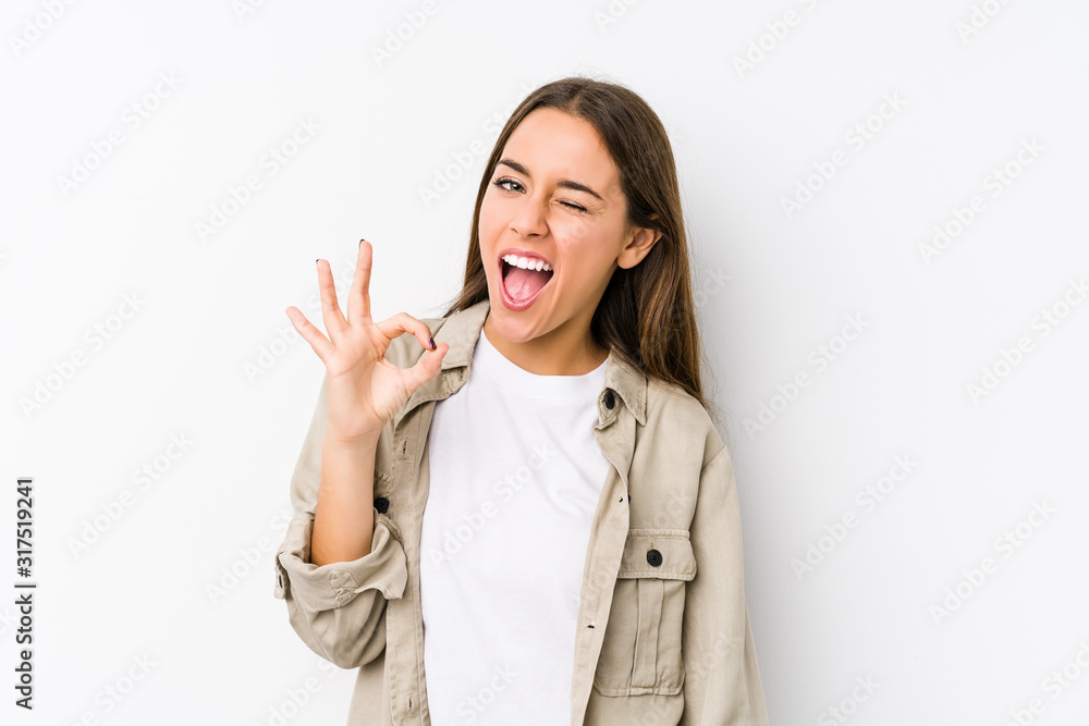 Young caucasian woman isolated winks an eye and holds an okay gesture with hand. Young caucasian woman isolated winks an eye and holds an okay gesture with hand.
