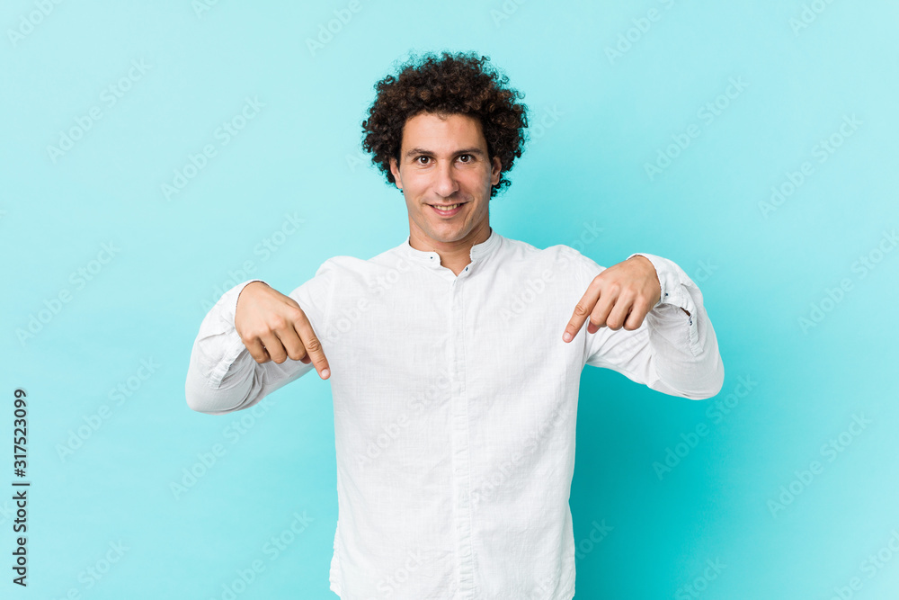 Young curly mature man wearing an elegant shirt points down with fingers, positive feeling. Young curly mature man wearing an elegant shirt points down with fingers, positive feeling.