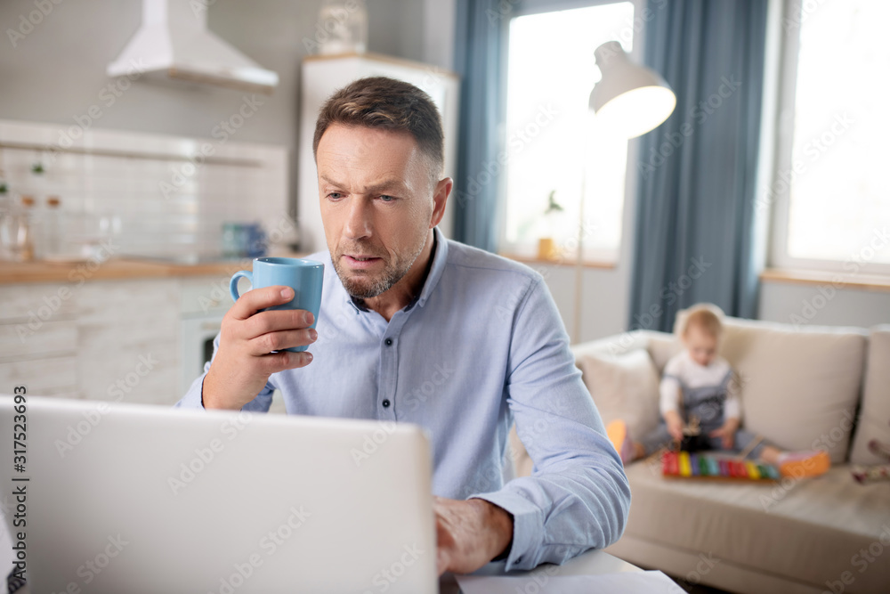 Bearded man in a blue shirt looking serious working on his laptop Bearded man in a blue shirt looking serious working on his laptop