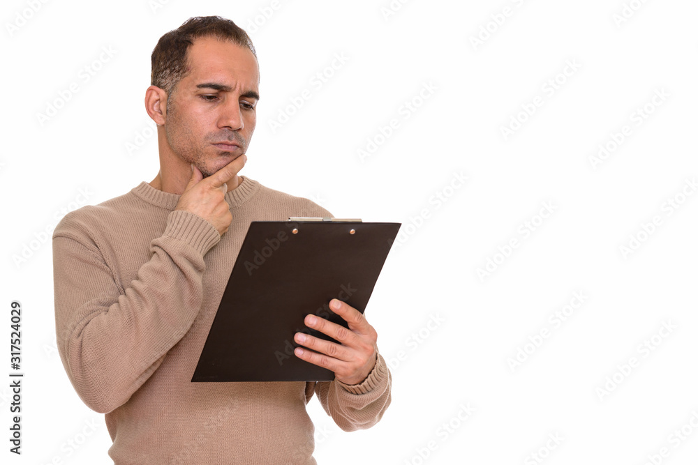 Mature handsome Persian man reading on clipboard while thinking Mature handsome Persian man reading on clipboard while thinking