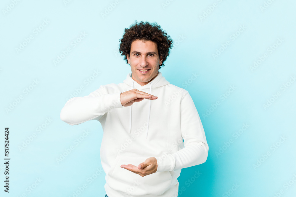 Young sporty man against a blue background holding something with both hands, product presentation. Young sporty man against a blue background holding something with both hands, product presentation.
