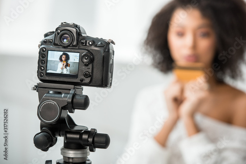 selective focus of digital camera with african american video blogger holding credit card on display
