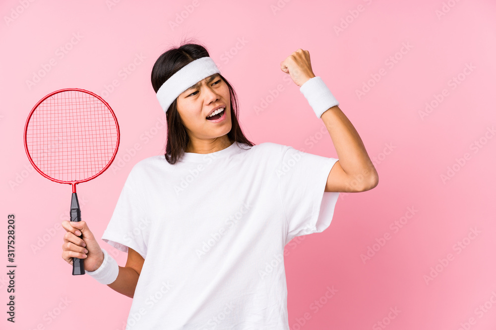 Young chinese woman playing badminton in a pink background raising fist after a victory, winner concept. Young chinese woman playing badminton in a pink background raising fist after a victory, winner concept.