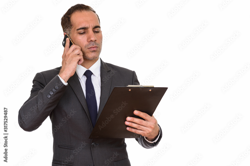Mature Persian businessman talking on the phone while reading on clipboard Mature Persian businessman talking on the phone while reading on clipboard