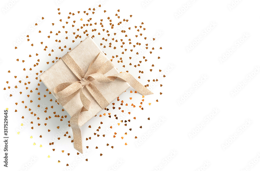 Beautiful present box with elegant golden bow on white background with gold heart sheped sparkles. Festive backdrop for your holiday design. Flat lay style.